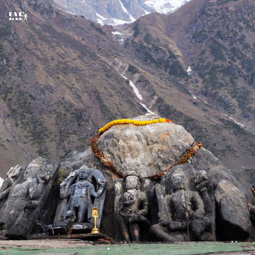 Ancient stone idols adorned with marigold garlands near Kedarnath Temple with Himalayan valley in the background.