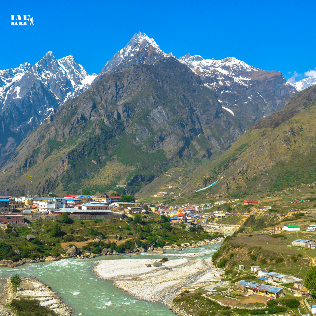 Badrinath town with Alaknanda River flowing through valley surrounded by snow-capped Himalayan peaks.