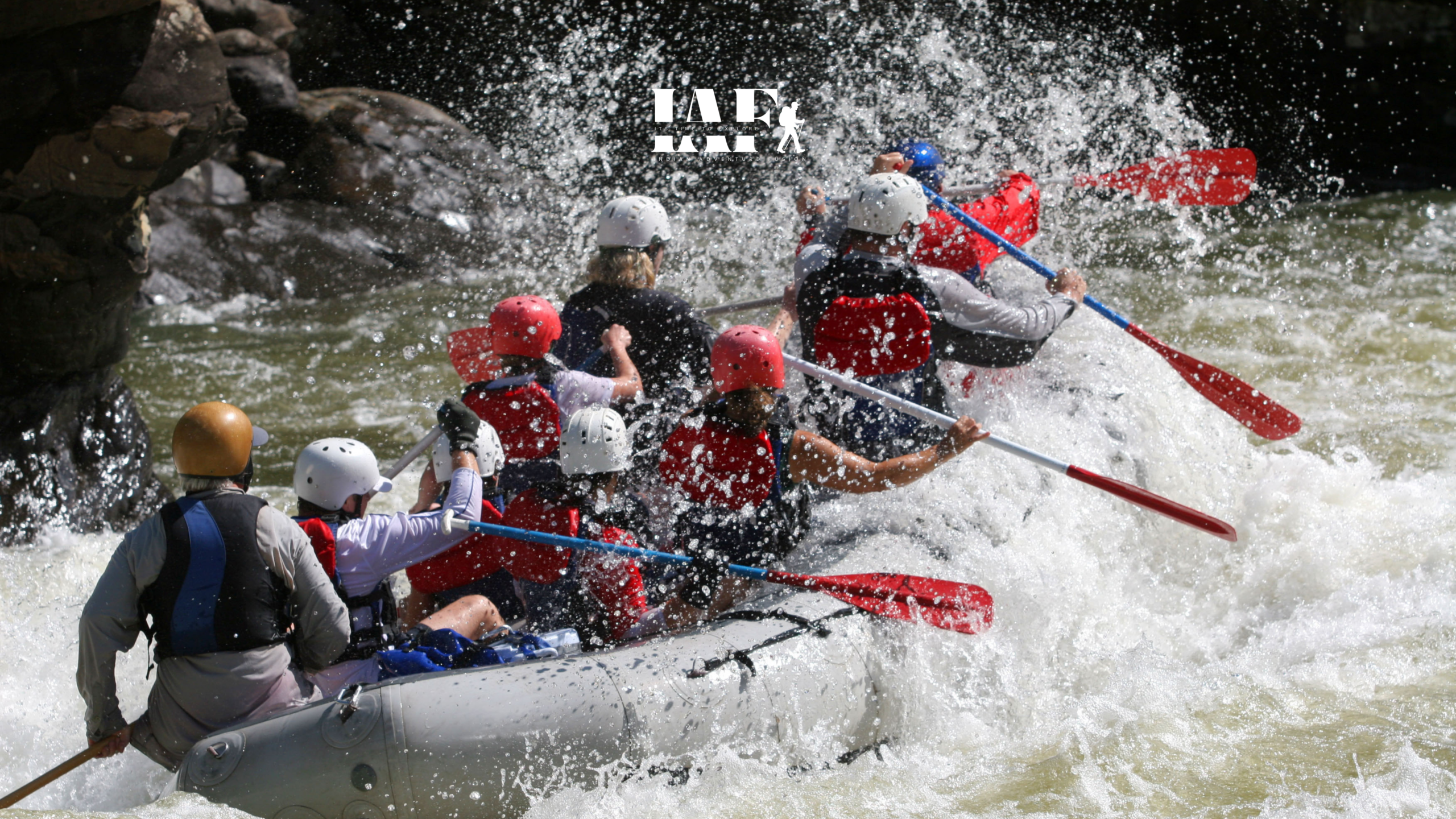 Group of people white water rafting in a river with helmets and life jackets during an adventure trip.