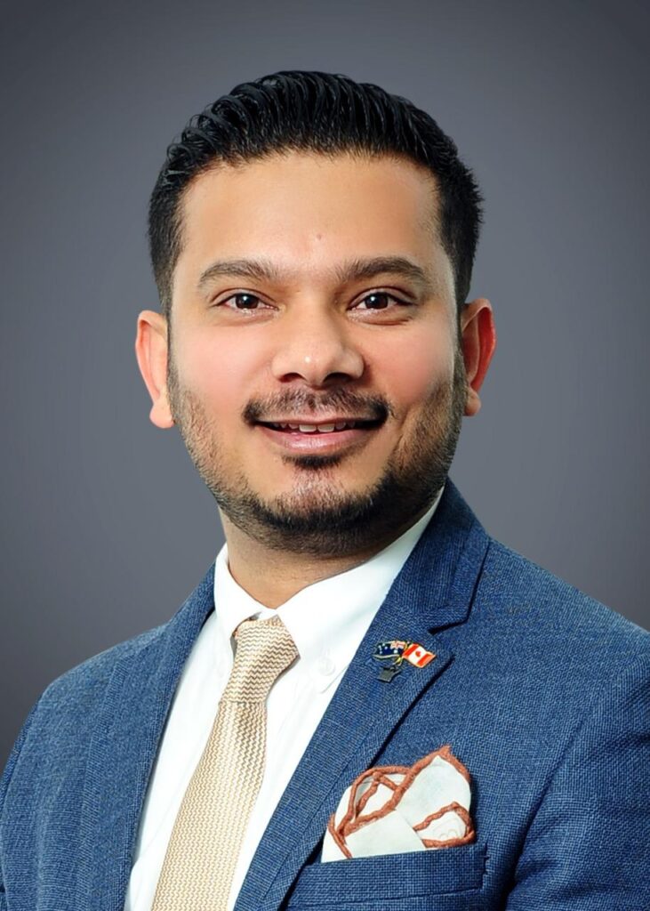 Portrait of Harish Chand, Co-Founder of Indian Adventure Fusion, wearing a blue blazer and beige tie against a grey background.